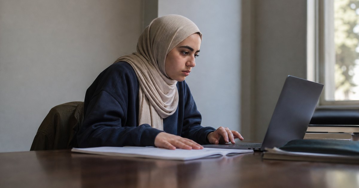 A woman in a headscarf reviews an order dashboard at a study table.