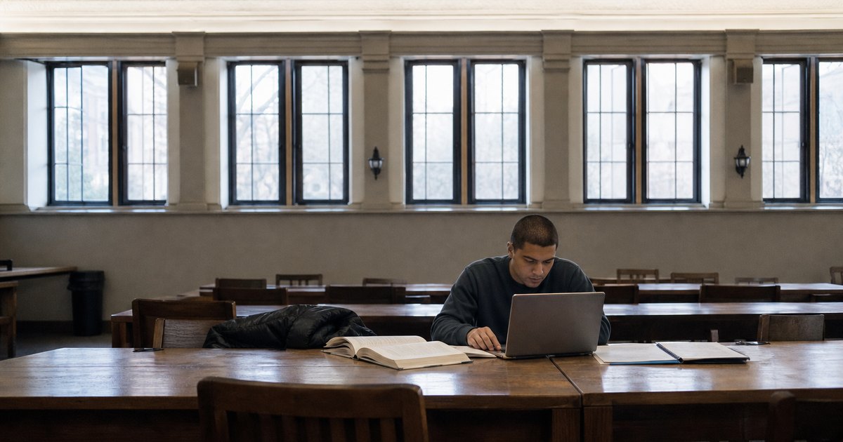 Student working alone at a laptop in a quiet library reading room.