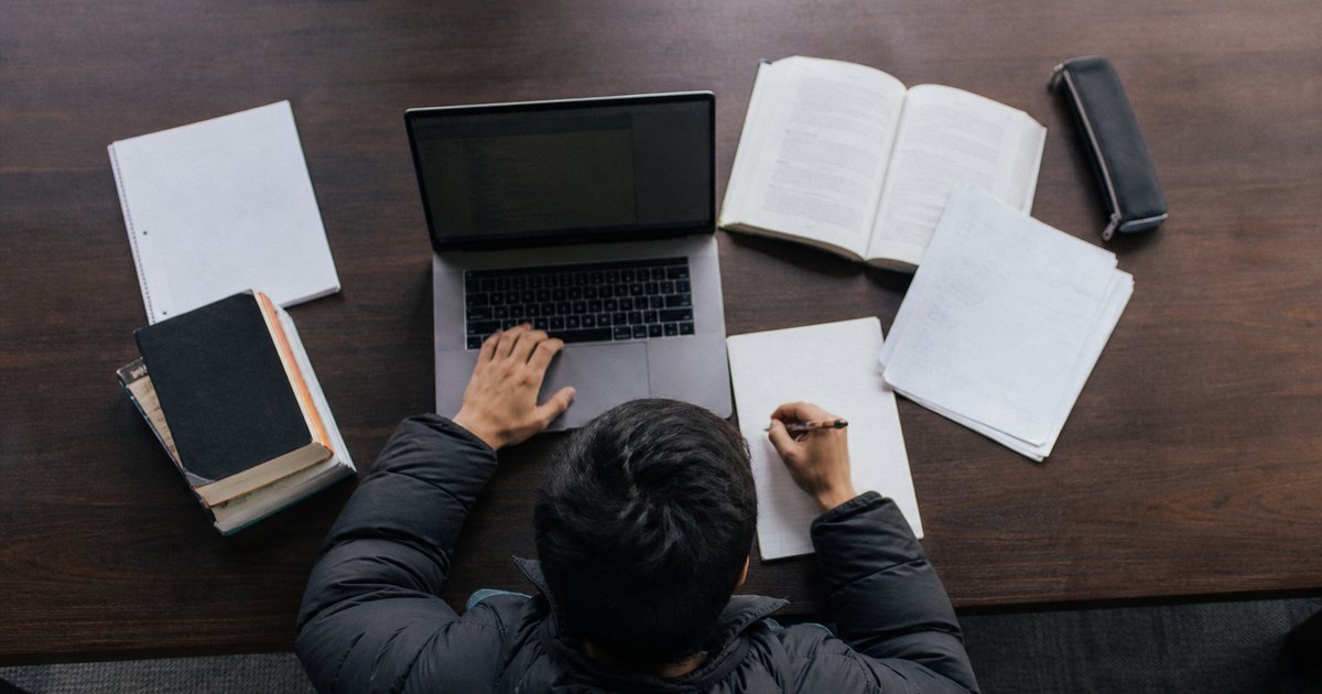 Student in a puffer jacket works over MBA notes and a laptop at a study table.