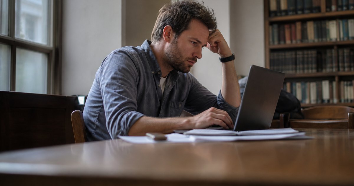 Adult student working on code at a laptop with notes spread across a study table.
